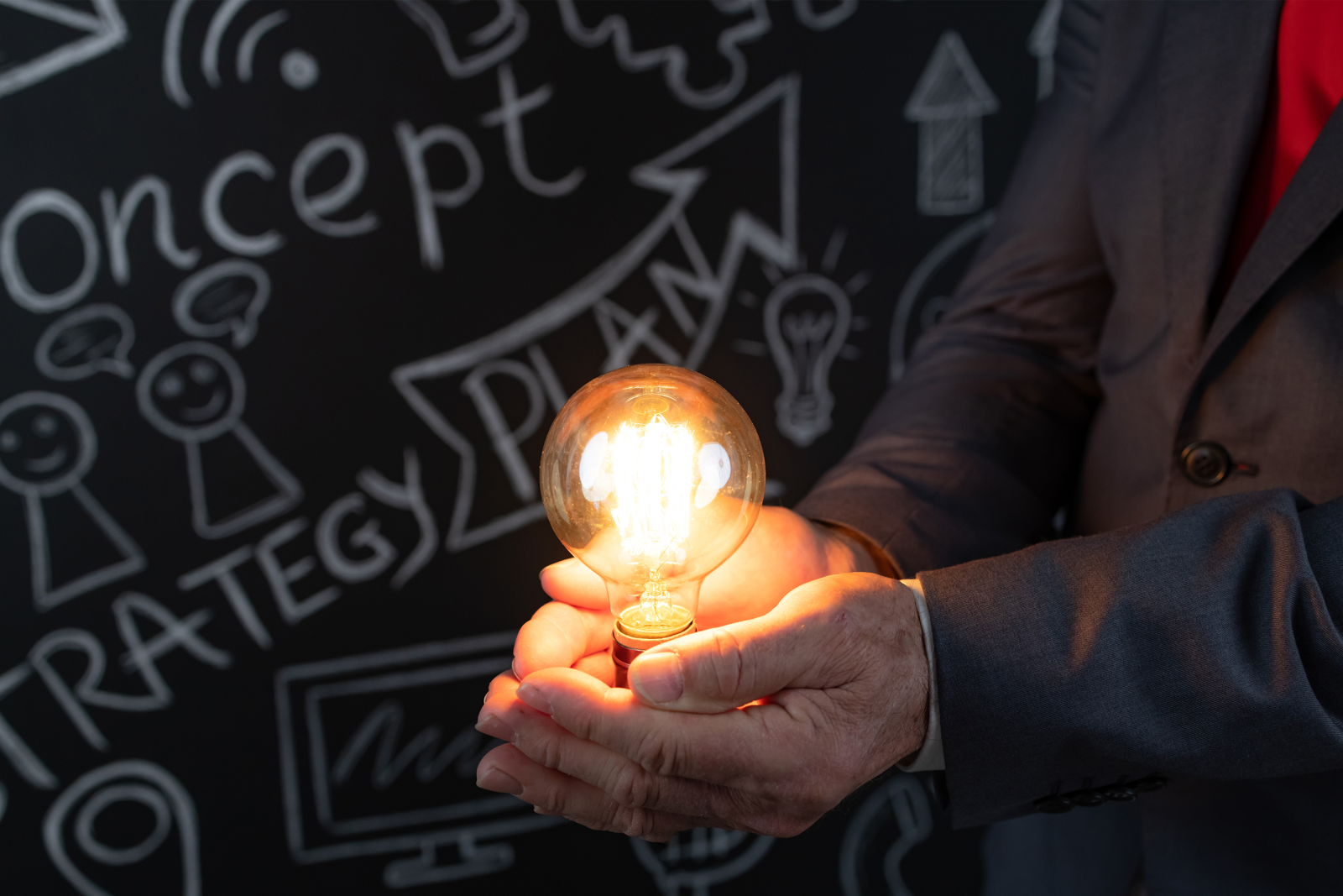 Man holding glowing lightbulb next to a blackboard with ideas on it