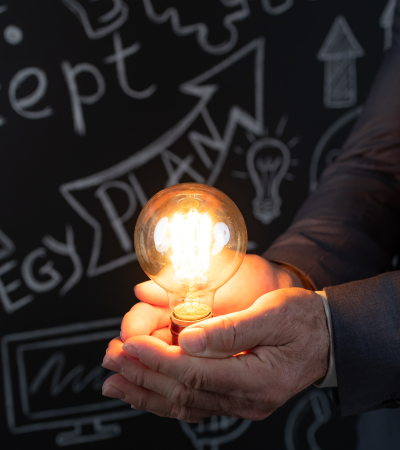 Man holding glowing lightbulb next to a blackboard with ideas on it